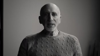 Movie still from “Stutz” (2022), directed by Jonah Hill – An older man wearing a gray sweater and smiling; Close Up shot, Low angle