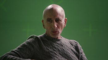 Movie still from “Stutz” (2022), directed by Jonah Hill – An older man with a bald head wearing a gray sweater; Close Up shot, Over the shoulder angle