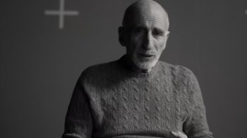 Movie still from “Stutz” (2022), directed by Jonah Hill – An older man wearing a sweater with a cross in the background; Close Up shot, Over the shoulder angle
