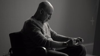 Movie still from “Stutz” (2022), directed by Jonah Hill – A man sitting in a chair writing on a piece of paper; Medium shot, Low angle