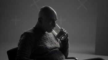 Movie still from “Stutz” (2022), directed by Jonah Hill – A bald man drinking from a glass with a straw in his mouth; Medium shot, Over the shoulder angle