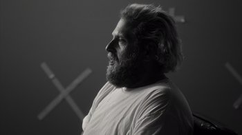 Movie still from “Stutz” (2022), directed by Jonah Hill – A man with long hair and a beard is looking to the side; Close Up shot, Over the shoulder angle