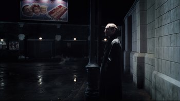 Movie still from “Charlie and the Chocolate Factory” (2005), directed by Tim Burton – A man standing next to a street pole in the dark at night; Wide shot, Over the shoulder angle