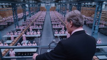 Movie still from “Charlie and the Chocolate Factory” (2005), directed by Tim Burton – A man in a black suit is standing in front of a room full of people; Wide shot, High angle