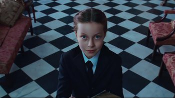 Movie still from “Charlie and the Chocolate Factory” (2005), directed by Tim Burton – A girl in a suit and tie holding a clipboard in front of checkerboard floor; Close Up shot, High angle