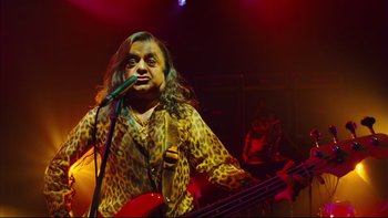 Movie still from “Charlie and the Chocolate Factory” (2005), directed by Tim Burton – A man with long hair is playing a guitar; Medium shot, Low angle