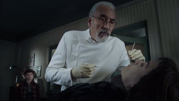 Movie still from “Charlie and the Chocolate Factory” (2005), directed by Tim Burton – An older man in a white shirt and white gloves is holding a needle; Close Up shot, Low angle