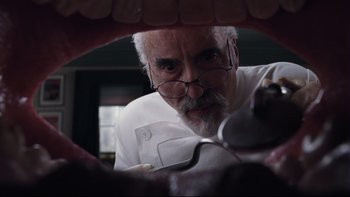 Movie still from “Charlie and the Chocolate Factory” (2005), directed by Tim Burton – An old man with a beard and glasses looking through a mouth; Extreme Close Up shot, Low angle