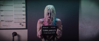 Movie still from “Suicide Squad” (2016), directed by David Ayer – A woman with blonde hair and pink and blue hair holding up a police sign; Medium shot, Low angle