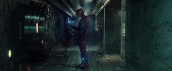 Movie still from “Suicide Squad” (2016), directed by David Ayer – A man dressed in a red and blue costume holding a cell phone; Wide shot, Low angle