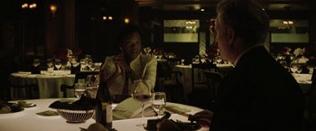 Movie still from “Suicide Squad” (2016), directed by David Ayer – A woman sitting at a table in front of a glass of wine; Medium shot, Over the shoulder angle