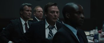 Movie still from “Suicide Squad” (2016), directed by David Ayer – A man in a suit and tie standing next to other men; Close Up shot, Low angle