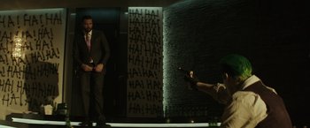 Movie still from “Suicide Squad” (2016), directed by David Ayer – A man in a suit and tie holding a gun; Wide shot, Over the shoulder angle