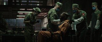 Movie still from “Suicide Squad” (2016), directed by David Ayer – A group of men in military fatigues are sitting in a room; Medium shot, Over the shoulder angle