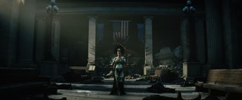 Movie still from “Suicide Squad” (2016), directed by David Ayer – A woman standing in front of an american flag and ruins; Wide shot, Low angle