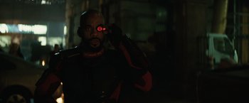 Movie still from “Suicide Squad” (2016), directed by David Ayer – A man in a black and red uniform holding a red object in front of his face; Close Up shot, Over the shoulder angle
