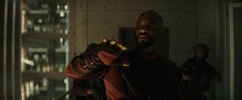 Movie still from “Suicide Squad” (2016), directed by David Ayer – A man in a red and green suit is holding his hands out; Close Up shot, Over the shoulder angle