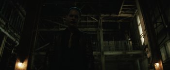 Movie still from “Suicide Squad” (2016), directed by David Ayer – A man in a suit and tie standing in a dark room; Medium shot, Over the shoulder angle