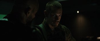 Movie still from “Suicide Squad” (2016), directed by David Ayer – A man in a dark room looking at the camera; Close Up shot, Over the shoulder angle