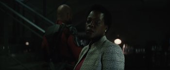 Movie still from “Suicide Squad” (2016), directed by David Ayer – A man standing next to another man in a dark room; Close Up shot, Over the shoulder angle
