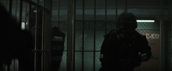 Movie still from “Suicide Squad” (2016), directed by David Ayer – A man in a black jacket standing in front of a metal gate; Wide shot, Low angle
