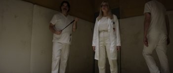 Movie still from “Suitable Flesh” (2023), directed by Joe Lynch – Two people dressed in white lab coats and white pants; Medium shot, Low angle