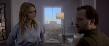 Movie still from “Suitable Flesh” (2023), directed by Joe Lynch – Two people are sitting in a living room talking; Medium shot, Over the shoulder angle