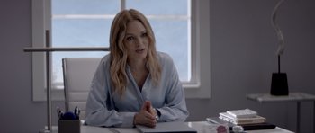 Movie still from “Suitable Flesh” (2023), directed by Joe Lynch – A woman sitting at a desk in front of a window; Medium shot, Over the shoulder angle