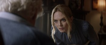 Movie still from “Suitable Flesh” (2023), directed by Joe Lynch – A woman looking into a mirror while standing in front of a wall; Close Up shot, Over the shoulder angle