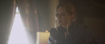 Movie still from “Suitable Flesh” (2023), directed by Joe Lynch – A woman with blonde hair wearing a black dress; Close Up shot, Over the shoulder angle