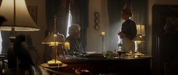 Movie still from “Suitable Flesh” (2023), directed by Joe Lynch – Two people sitting at a table in a room with candles; Medium shot, Over the shoulder angle