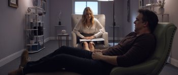 Movie still from “Suitable Flesh” (2023), directed by Joe Lynch – A woman sitting in a chair in front of a man; Wide shot, Over the shoulder angle