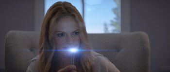 Movie still from “Suitable Flesh” (2023), directed by Joe Lynch – A woman is holding a light in front of her face; Close Up shot, Over the shoulder angle
