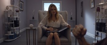 Movie still from “Suitable Flesh” (2023), directed by Joe Lynch – A woman sitting in a chair holding a laptop; Medium shot, Over the shoulder angle