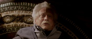 Movie still from “Suitable Flesh” (2023), directed by Joe Lynch – An old man with white hair and a gray jacket; Close Up shot, Overhead angle