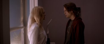 Movie still from “Suitable Flesh” (2023), directed by Joe Lynch – A woman and a man standing next to each other in front of a window; Medium shot, Over the shoulder angle