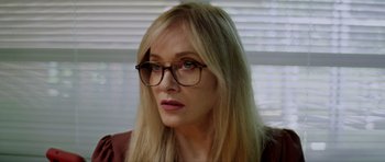 Movie still from “Suitable Flesh” (2023), directed by Joe Lynch – A woman wearing glasses and looking at the camera; Close Up shot, Over the shoulder angle