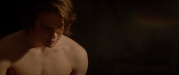 Movie still from “Suitable Flesh” (2023), directed by Joe Lynch – A man with long brown hair and a bare chest; Close Up shot, Over the shoulder angle