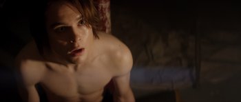 Movie still from “Suitable Flesh” (2023), directed by Joe Lynch – A shirtless man with long brown hair is looking at the camera; Close Up shot, High angle