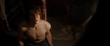Movie still from “Suitable Flesh” (2023), directed by Joe Lynch – A shirtless man standing next to a pole; Medium shot, Low angle