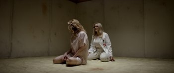 Movie still from “Suitable Flesh” (2023), directed by Joe Lynch – Two women sitting on the ground in a room; Wide shot, High angle