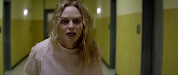 Movie still from “Suitable Flesh” (2023), directed by Joe Lynch – A woman in a pink polka dot shirt is looking at the camera; Close Up shot, Over the shoulder angle