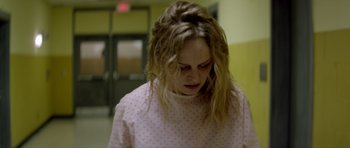 Movie still from “Suitable Flesh” (2023), directed by Joe Lynch – A woman in a pink polka dot shirt looking down; Medium shot, Over the shoulder angle