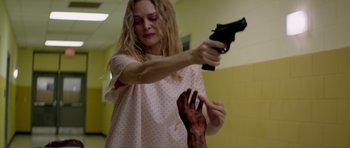 Movie still from “Suitable Flesh” (2023), directed by Joe Lynch – A woman holding a gun and a hand with blood coming out of it; Medium shot, Over the shoulder angle