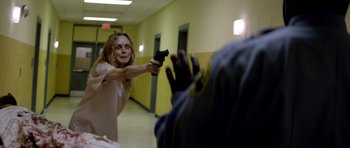 Movie still from “Suitable Flesh” (2023), directed by Joe Lynch – A woman holding a gun in her hand in a hallway; Medium shot, Over the shoulder angle