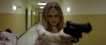 Movie still from “Suitable Flesh” (2023), directed by Joe Lynch – A woman holding a gun in a hallway; Close Up shot, Low angle