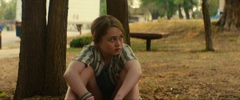 Movie still from “Summering” (2022), directed by James Ponsoldt – A girl sitting on the ground near a tree in a park; Medium shot, Over the shoulder angle