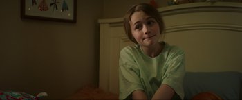 Movie still from “Summering” (2022), directed by James Ponsoldt – A young girl sitting on a chair in a room; Close Up shot, Over the shoulder angle