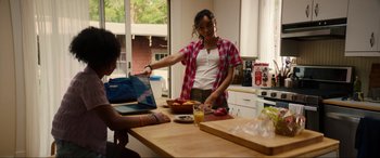 Movie still from “Summering” (2022), directed by James Ponsoldt – A woman standing at a table with a laptop; Medium shot, Over the shoulder angle