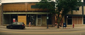 Movie still from “Summering” (2022), directed by James Ponsoldt – A woman walking down the street in front of a building; Extreme Wide shot, Low angle
